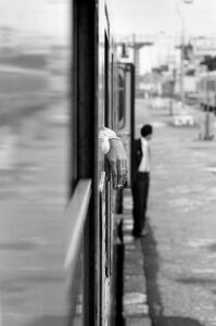 Photo Art Street Photography. En gare, depuis une fenêtre de train, mise en relation entre une femme que l'on devine et un homme dans l'attente