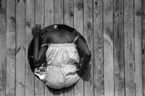 Photo Art Street Photography. Paris. Une jeune fille black de dos apparait dans une ouverture de palissade Parc Georges Brassens.